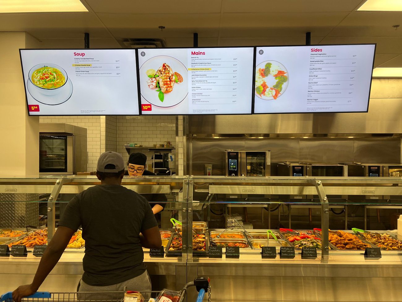 The Farm & Fare hot counter with digital menu boards and a customer being served